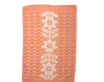 May include: A peach-colored hand towel with a white floral design. The towel has a textured surface and a decorative border.