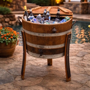 May include: A wooden barrel cooler filled with ice, bottles of beer, and water bottles. The cooler has a hinged lid and is supported by curved wooden legs. A bottle opener is attached to the side. The cooler is outdoors near a pool.