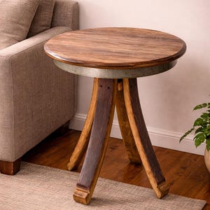 May include: A round wooden side table with a dark brown tabletop and three curved legs. The tabletop is approximately 24 inches in diameter and is supported by a metal band. The legs are made of dark wood and are angled outwards.