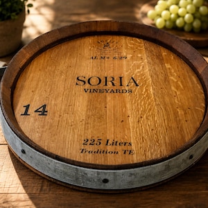 May include: A round wooden serving tray crafted from a wine barrel head, featuring a dark wood rim, a galvanized metal band, and two metal handles. The surface is printed with SORIA VINEYARDS, the number 14, and the text 225 Liters Tradition TE.