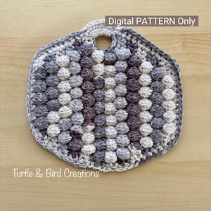 May include: A crochet pot holder with a handle in a hexagonal shape. The pot holder is made with a textured stitch in shades of gray, white, and purple. The text "Digital PATTERN Only" is at the top of the image. The text "Turtle & Bird Creations" is at the bottom of the image.