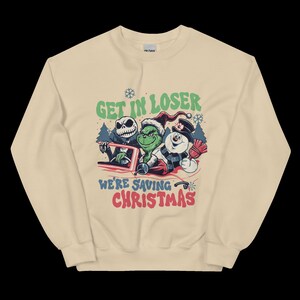 May include: Beige crewneck sweatshirt with a graphic featuring Jack Skellington, the Grinch, and a snowman in a car. Text reads "GET IN LOSER" above and "WE'RE SAVING CHRISTMAS" below the characters. A fun, festive design for the holiday season.