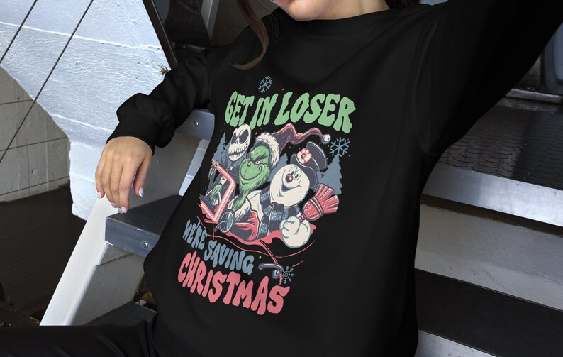 May include: Black sweatshirt featuring a graphic with the text "GET IN LOSER WE'RE SAVING CHRISTMAS." The graphic includes cartoon characters Jack Skellington, The Grinch, and a snowman. The design has a vintage, distressed look.