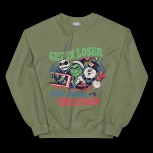 May include: Olive green sweatshirt with a graphic featuring Jack Skellington, the Grinch, and a snowman. Text reads "GET IN LOSER WE'RE SAVING CHRISTMAS" in green, red, and blue. The sweatshirt has a crew neck and long sleeves.