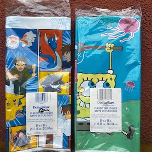 May include: Two plastic tablecloths in packaging. One features Pokémon characters, the other SpongeBob SquarePants. Each measures 54 x 96 inches (137.16 cm x 243.84 cm). The Pokémon tablecloth has a blue, red, and yellow design.