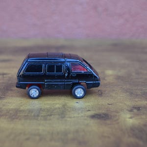 May include: A black toy van with red tinted windows. The van is sitting on a wooden surface.