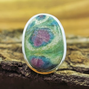 May include: A silver ring featuring a large oval green, blue and pink gemstone. The gemstone has a swirling pattern.