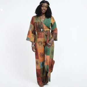 May include: A patchwork-style two-piece outfit in shades of orange, green, and brown. The top is a wrap-style with wide sleeves, and the pants are wide-legged. The fabric features floral and geometric patterns. The outfit is accessorized with jewelry.