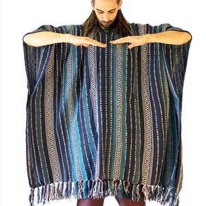 May include: A dark blue and teal poncho featuring vertical stripes with white geometric patterns and a fringe hem. The garment has a wide, loose-fitting silhouette with short sleeves and a textured woven fabric construction throughout the piece.