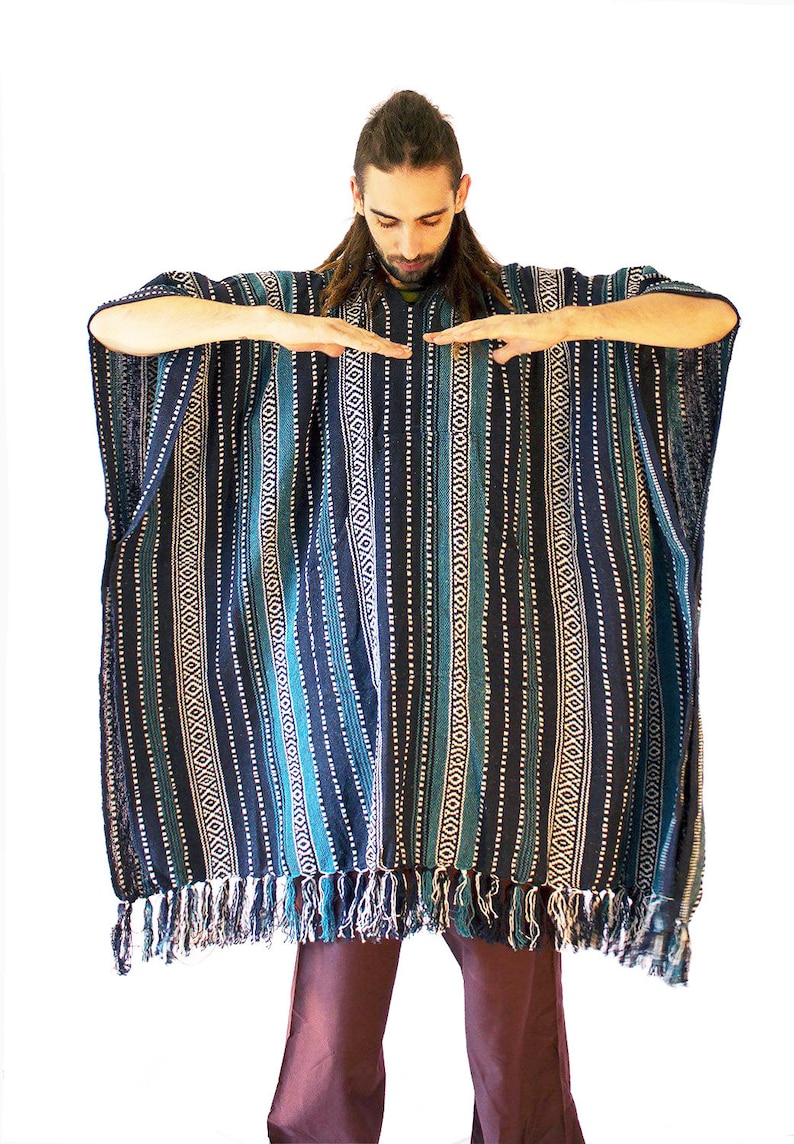 May include: A dark blue and teal poncho featuring vertical stripes with white geometric patterns and a fringe hem. The garment has a wide, loose-fitting silhouette with short sleeves and a textured woven fabric construction throughout the piece.