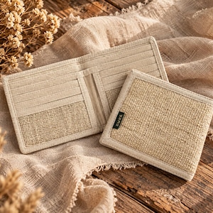 May include: A beige bifold wallet made of woven natural fiber and fabric, featuring multiple interior card slots and a small dark green rectangular tag with white text on the exterior. The wallet is shown both open and closed.
