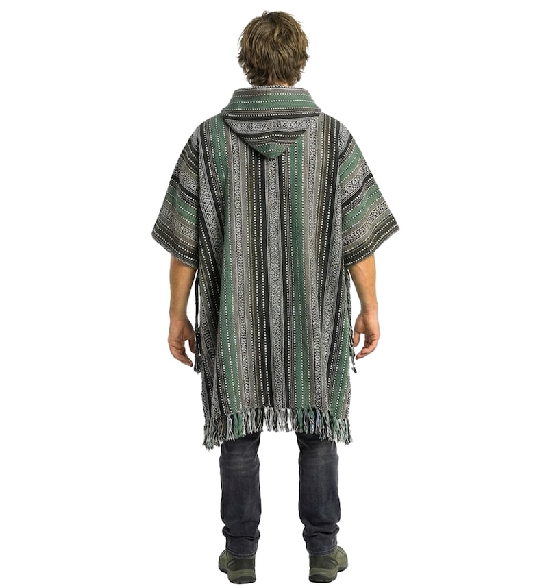 May include: A hooded poncho featuring a vertical striped pattern in shades of forest green, black, white, and grey. The garment has short sleeves, a hood, and a fringed hemline at the bottom. It is worn over dark grey jeans and dark shoes.