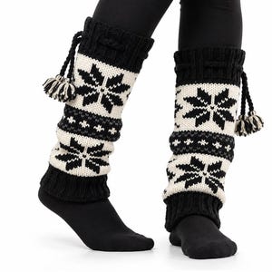 May include: A pair of black and white knit leg warmers featuring a repeating snowflake pattern, a ribbed cuff at the top and bottom, and a decorative drawstring cord with two small pom-poms hanging from the side of each leg warmer.