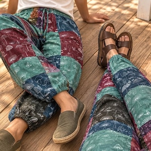 May include: Patchwork pants featuring a repeating mushroom and botanical print in shades of teal, burgundy, and dark blue. The pants have an elastic waistband with a drawstring and elasticized cuffs at the ankles, worn with olive slip-on shoes.