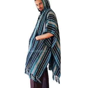 May include: A hooded poncho in shades of dark blue, teal, and white, featuring a repeating geometric pattern of horizontal stripes and diamond shapes. The garment includes a front pocket and a fringed hem along the bottom edge.
