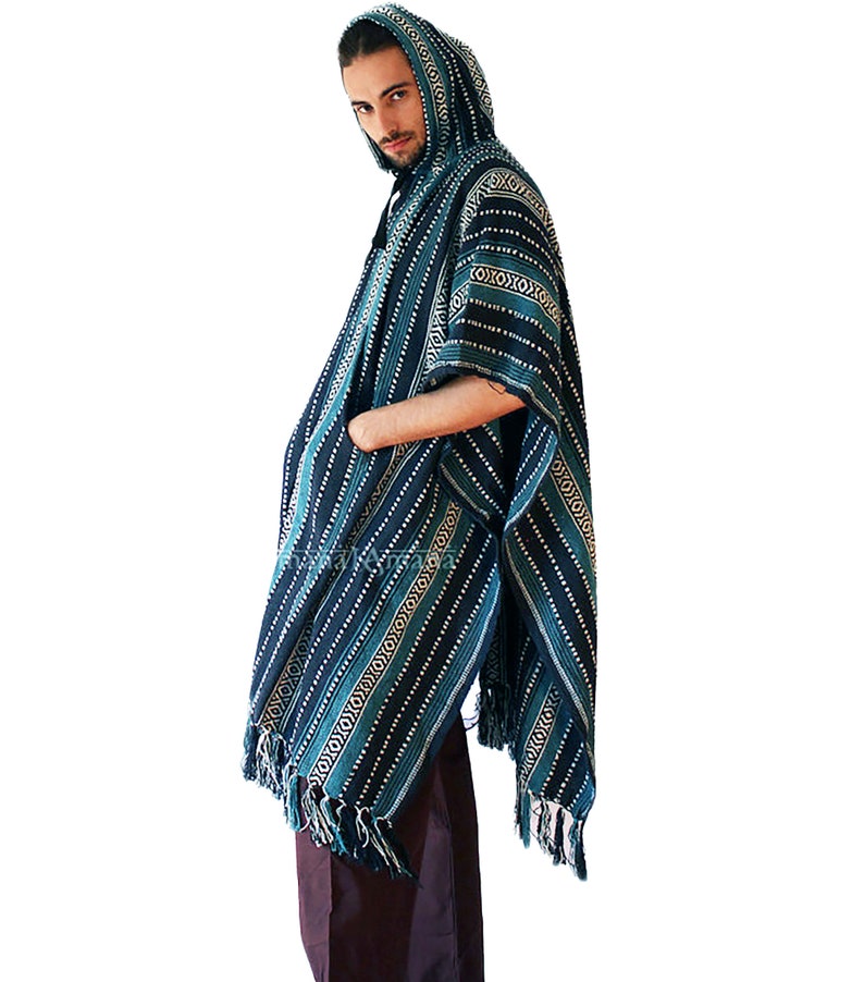 May include: A hooded poncho in shades of dark blue, teal, and white, featuring a repeating geometric pattern of horizontal stripes and diamond shapes. The garment includes a front pocket and a fringed hem along the bottom edge.