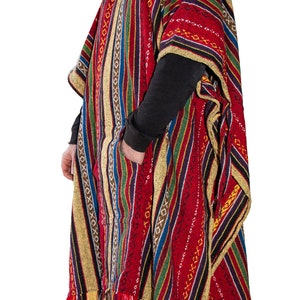 May include: A hooded poncho featuring a vibrant, multi-colored striped pattern in shades of red, gold, blue, and black. The garment includes a front pocket, a drawstring hood, and a fringed hemline, showcasing a woven texture throughout the fabric.