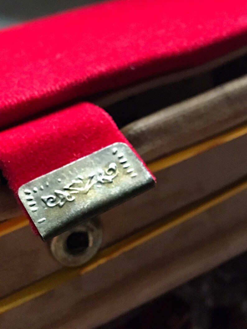 K&ouml;nnte beinhalten: Nahaufnahme eines roten Samtstoffs mit einem Metallverschluss. Der Verschluss hat ein eingraviertes Design und ist an einer Holzstruktur befestigt. Das Bild hebt die Textur und die Details der Materialien hervor.