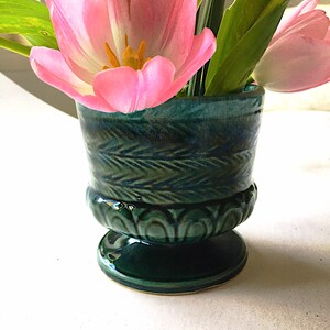 May include: A green ceramic vase with a decorative design, holding pink tulips.