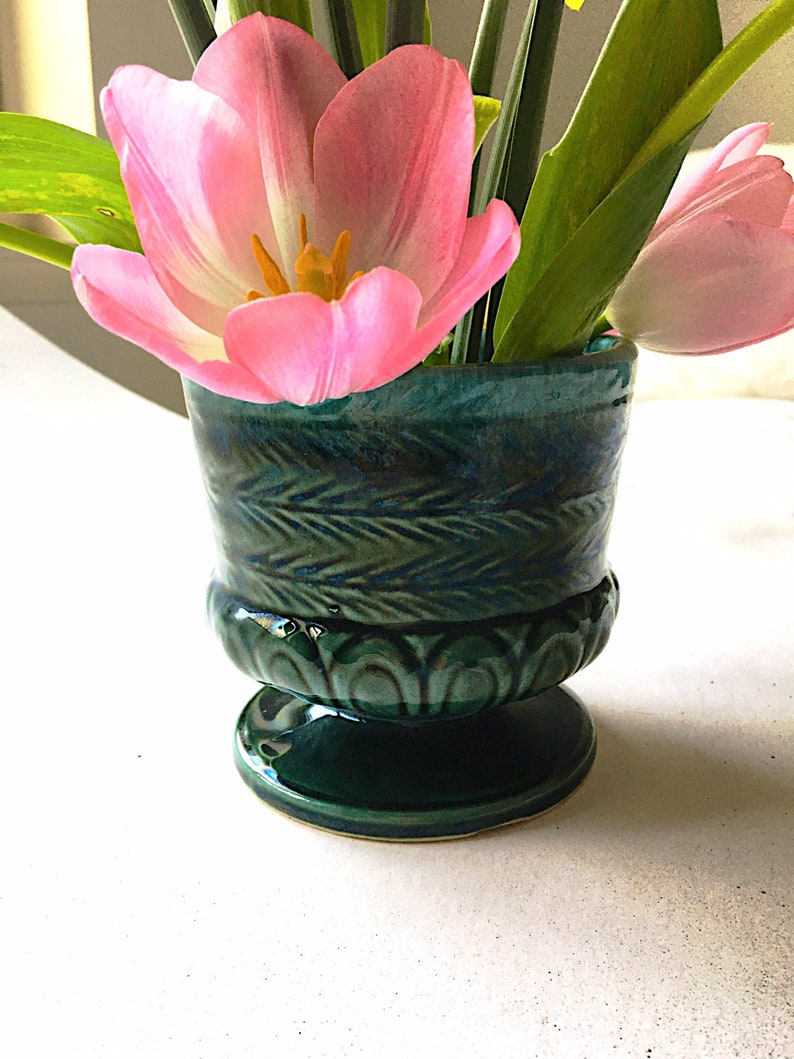 May include: A green ceramic vase with a decorative design, holding pink tulips.