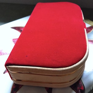 K&ouml;nnte beinhalten: Eine rechteckige rote Samtbox mit abgerundeter Oberseite. Die Box hat einen hellbeigen Rand mit einer d&uuml;nnen goldenen Zierleiste. Die Box liegt auf einer gemusterten Oberfl&auml;che.