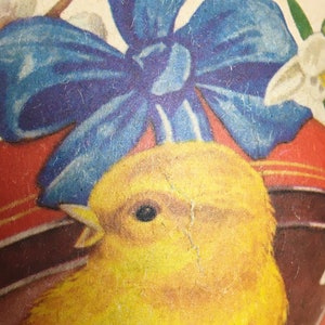May include: A vintage Easter egg with a yellow chick and a blue bow. The egg is decorated with white flowers and a red and white striped band.