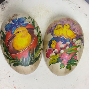 May include: Two vintage Easter eggs decorated with paper. One egg features a yellow chick in a red nest with blue ribbon and flowers. The other egg has two yellow chicks with blue ribbon and pink flowers.