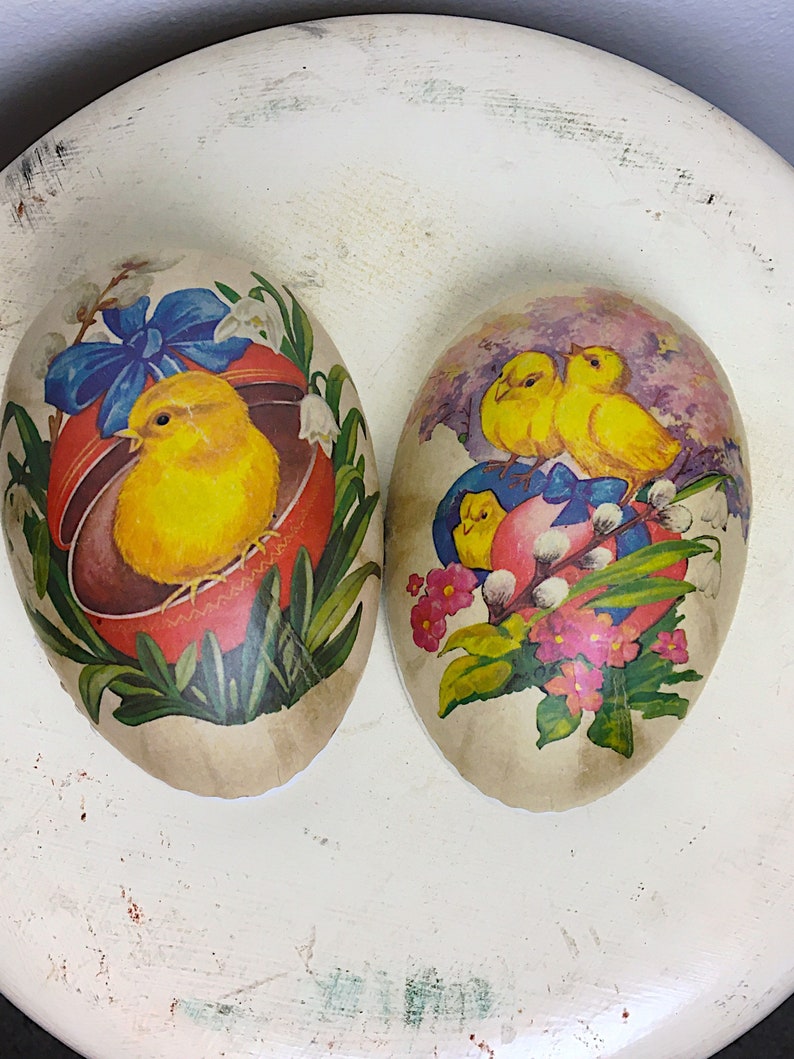 May include: Two vintage Easter eggs decorated with paper. One egg features a yellow chick in a red nest with blue ribbon and flowers. The other egg has two yellow chicks with blue ribbon and pink flowers.
