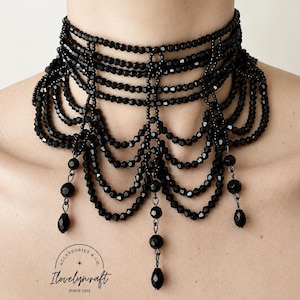Könnte beinhalten: Eine mehrreihige schwarze Perlenhalskette mit facettierten Perlen in einem drapierten, bogenförmigen Design mit drei hängenden Perlenakzenten. Das Bild enthält ein kreisförmiges Logo mit dem Text Accessories & Co. Ilovelynraft Since 2012.