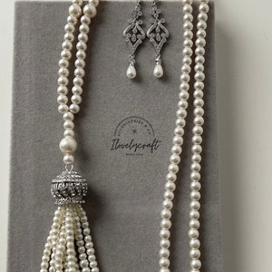 May include: A white pearl necklace with a crystal tassel pendant and matching crystal earrings. The necklace is on a gray background.