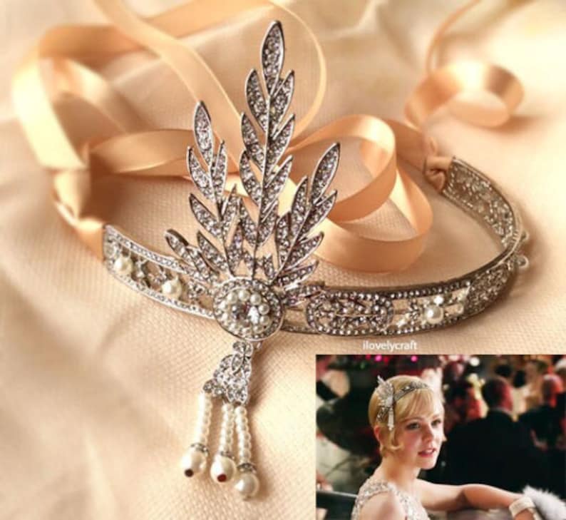 May include: A silver headband with a delicate floral design and pearl accents. The headband is adorned with sparkling rhinestones and features a dangling pearl and rhinestone drop.