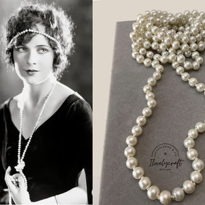 May include: A long strand of white faux pearl beads in a box. The beads are strung on a thin wire and are about 1/2 inch in diameter. The box is gray and has the text "Accessories & Co. Lovelycraft since 2014" printed on it.