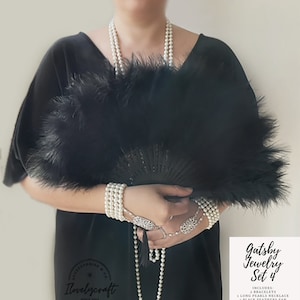 K&ouml;nnte beinhalten: Gatsby Schmuck Set 4 beinhaltet zwei Perlenarmb&auml;nder, eine lange Perlenkette und einen schwarzen Federf&auml;cher.