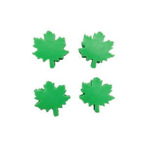May include: Four green maple leaf shaped embellishments. The leaves are made of a smooth, solid material.