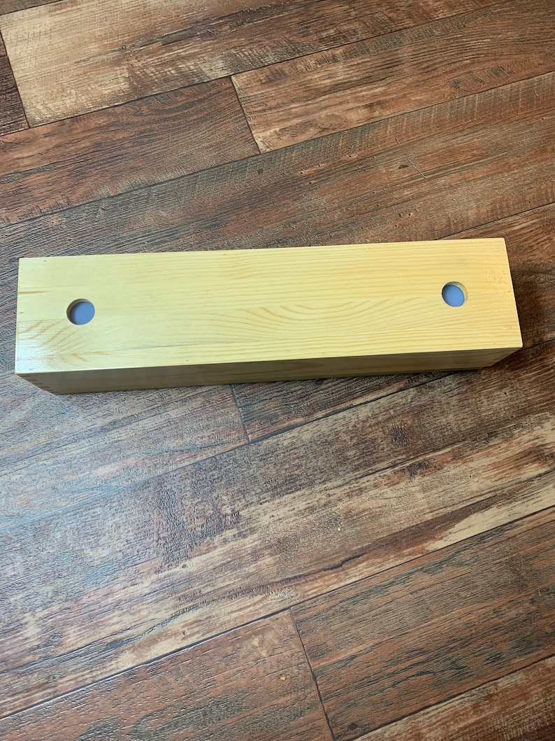 Puede incluir: Una caja de madera clara con dos agujeros en la parte superior. La caja est&aacute; sobre un suelo de madera.