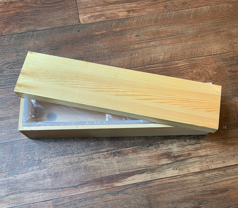 Puede incluir: Una caja de madera con tapa abatible y un forro de pl&aacute;stico transparente. La caja est&aacute; hecha de madera clara y tiene un acabado natural.
