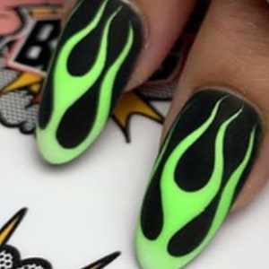 May include: Close-up of two fingernails with black and green flame designs. The nails are long and oval shaped.