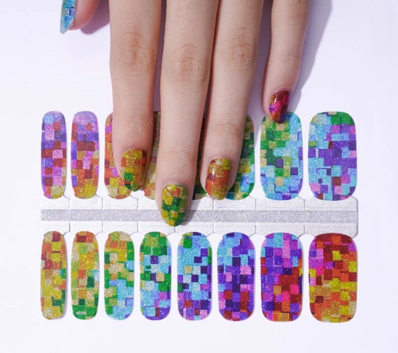 May include: A set of colorful nail wraps with a mosaic design. The wraps feature a glittery finish and a pattern of small squares in shades of yellow, green, blue, purple, and red. The nail wraps are shown on a white surface.