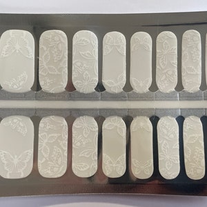 May include: A sheet of pale grey nail wraps with a butterfly design. The wraps feature a repeating pattern of white butterflies in various sizes and orientations. The nail wraps are packaged in a silver foil packet.