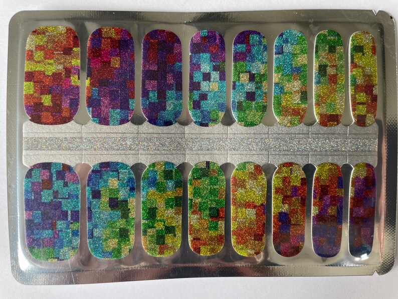May include: Nail polish strips with a colorful, glittery mosaic pattern. The strips are arranged in a silver package, featuring a variety of colors including red, green, blue, and purple. The design is made up of small squares.