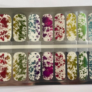 May include: A sheet of 12 nail wraps with a splatter paint design in various colors, including red, green, blue, and purple. The wraps are packaged in a silver and white plastic container.