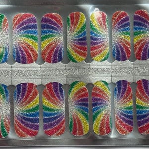 Può includere: Un foglio di nail wrap glitterati arcobaleno. Ogni wrap presenta un design a spirale in rosso, arancione, giallo, verde, blu e viola. Le wrap sono disposte su due file, con un supporto argentato.