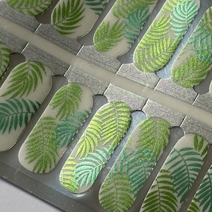 Puede incluir: Envolturas de u&ntilde;as con un dise&ntilde;o de hojas de palmera tropicales en tonos verdes y purpurina plateada. Las envolturas de u&ntilde;as est&aacute;n sobre un fondo transparente, con un respaldo plateado. Las envolturas de u&ntilde;as est&aacute;n en un paquete rectangular.