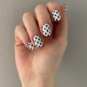 Könnte beinhalten: Nahaufnahme einer Hand mit weißem Nagellack mit schwarzen Punkten.