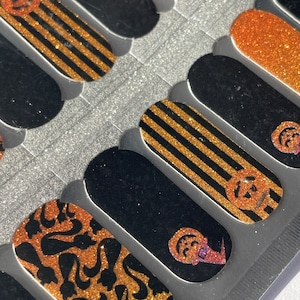May include: A sheet of black and gold Halloween nail decals with various designs, including pumpkins, stripes, and swirls.