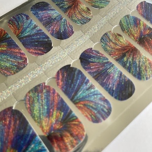 Può includere: Un foglio di adesivi per unghie con un design colorato e iridescente. Ogni adesivo presenta un'esplosione di colore, tra cui sfumature di blu, arancione e verde, che si irradiano da un punto centrale. Gli adesivi sono su un supporto argentato.