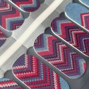May include: Nail wraps featuring a chevron design in shades of blue, pink, and purple. The pattern resembles a knitted sweater.