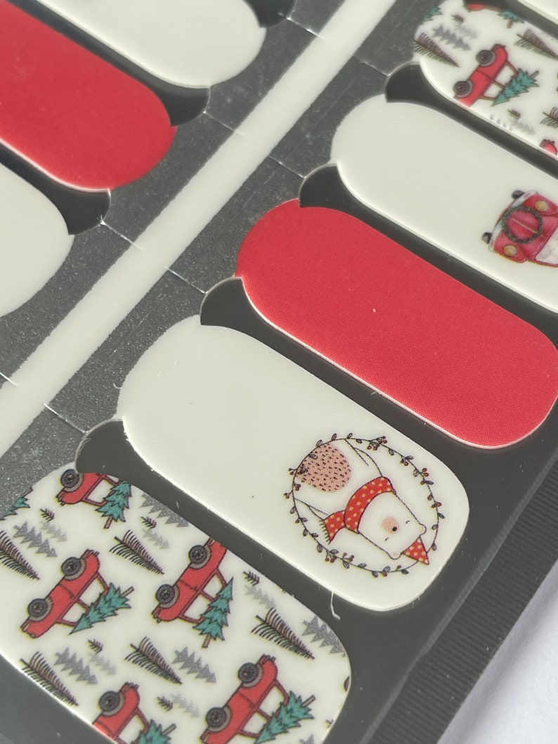 May include: A sheet of nail polish strips featuring a festive Christmas theme. Designs include red and white patterns, a polar bear wearing a scarf, and red trucks carrying Christmas trees. The strips are in various sizes.