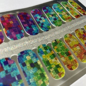 May include: A set of nail polish strips with a colorful, pixelated design. The strips feature a glittery finish and a variety of colors, including red, purple, blue, green, and yellow. The nail art is arranged in a clear plastic package.