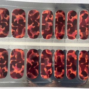 May include: A sheet of nail wraps with a tortoise shell pattern in shades of brown, orange, and red. The wraps are packaged in a clear plastic sheet with a silver backing.